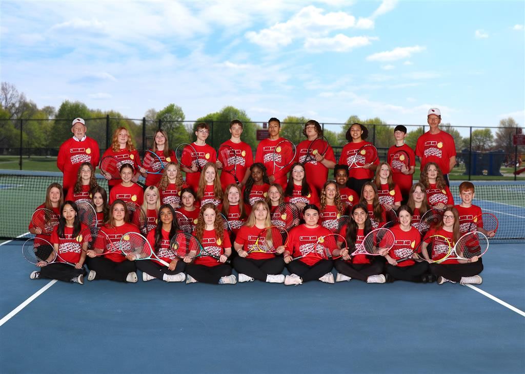 The girls tennis team smiling together for a group photo, showcasing their unity and love for the sport.