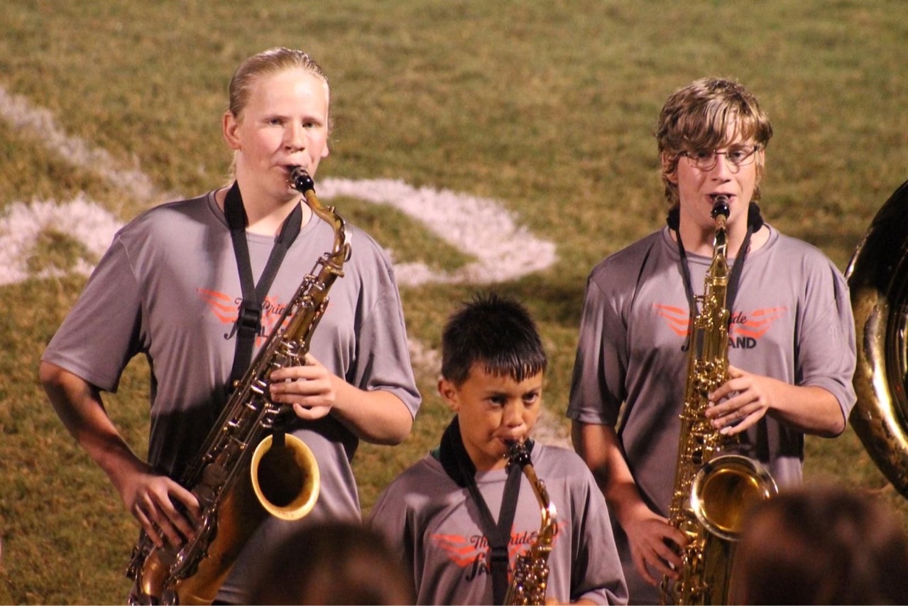 A photo of three students playing a saxophone