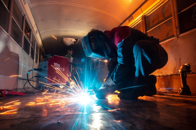 A man welding on a bus in a workshop.