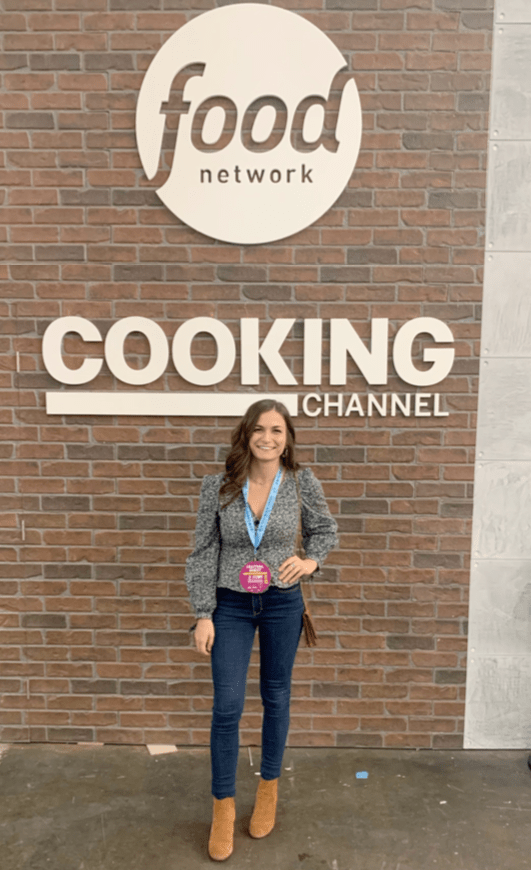 Woman standing in front of sign reading "Food Network Cooking Channel".
