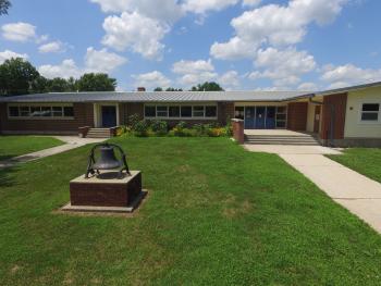 school building with green grass and bell in front