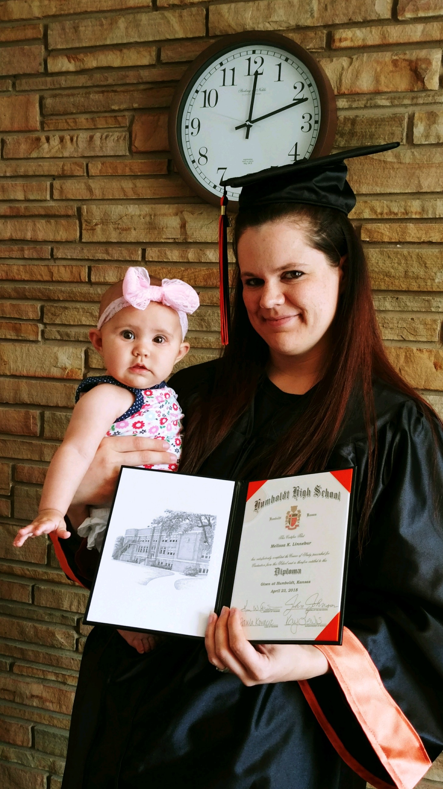 student holding a diploma and her baby