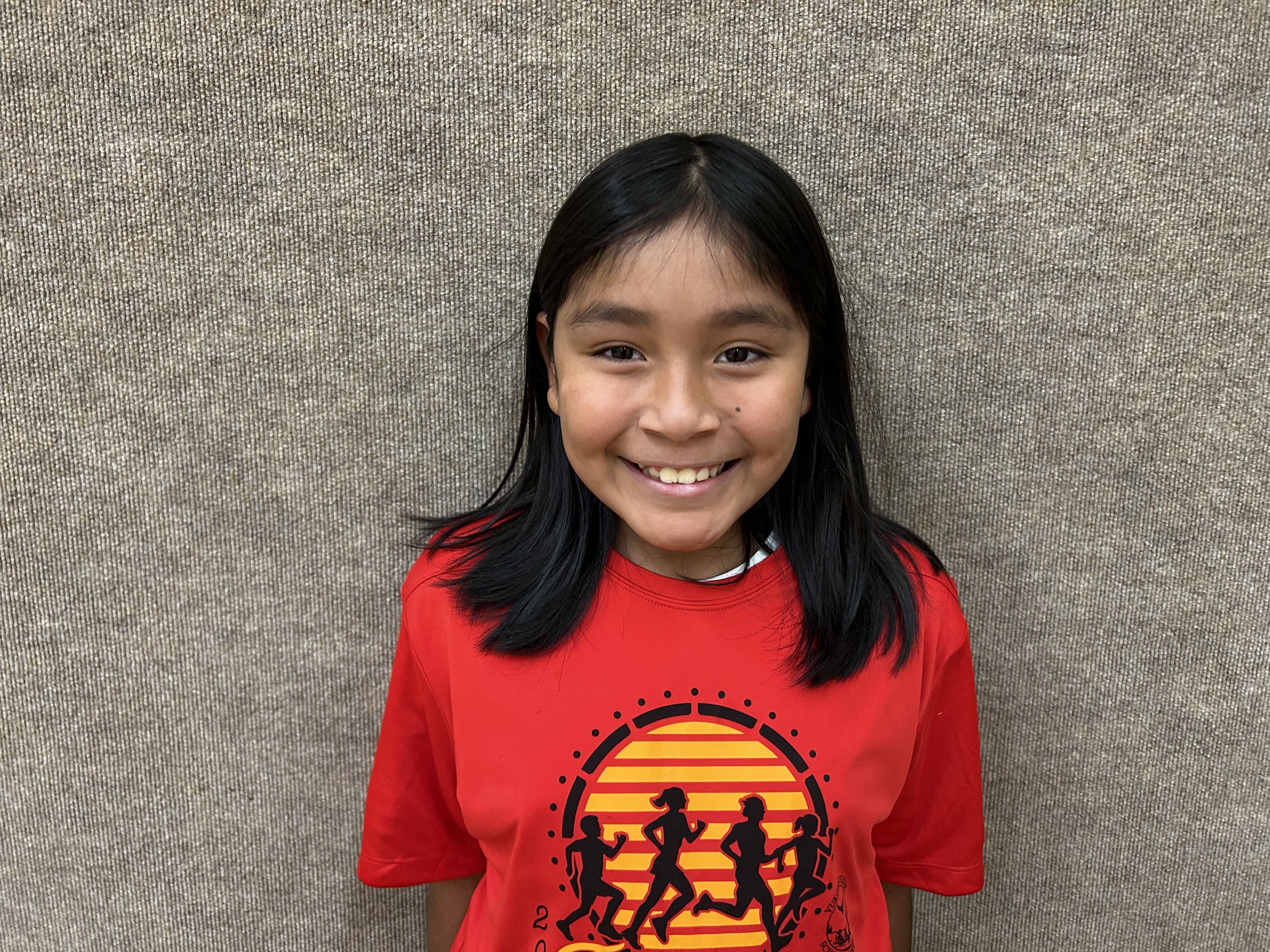 A young girl in a red shirt with the sun in the background.