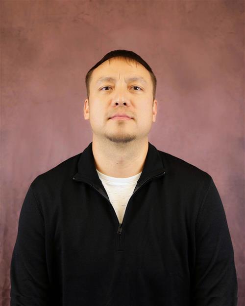 Man in black shirt standing against purple wall.