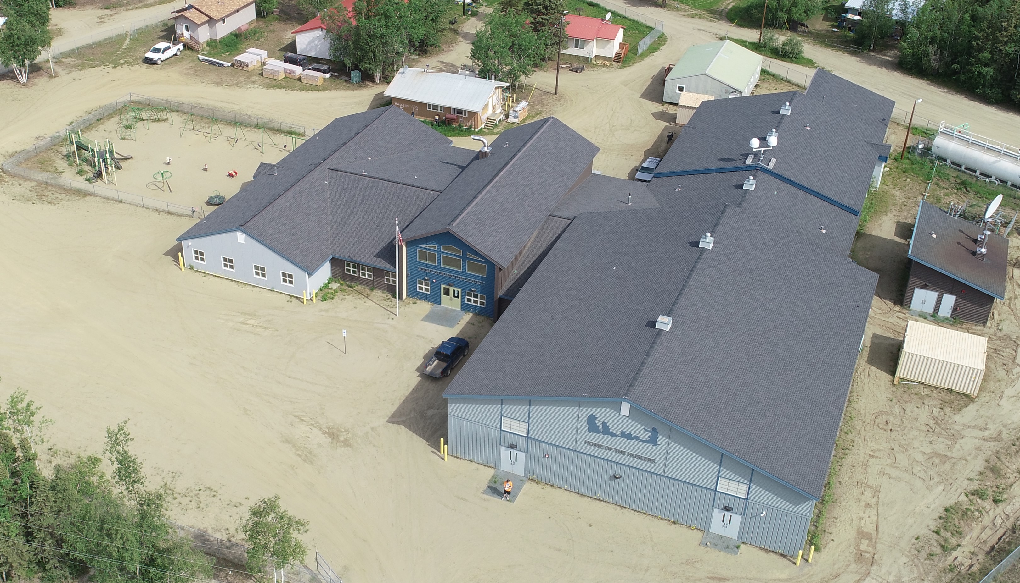 The image shows an aerial view of a group of buildings in a rural area. The buildings are all different shapes and sizes, and they are surrounded by dirt and grass. 