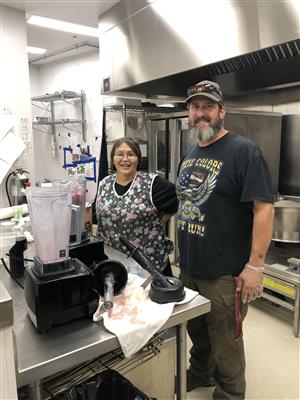 Two individuals in a kitchen, one operating a blender.