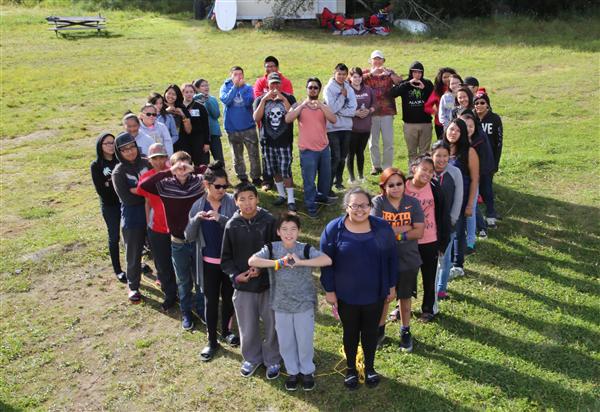 Group of people forming a heart shape on a grassy field.