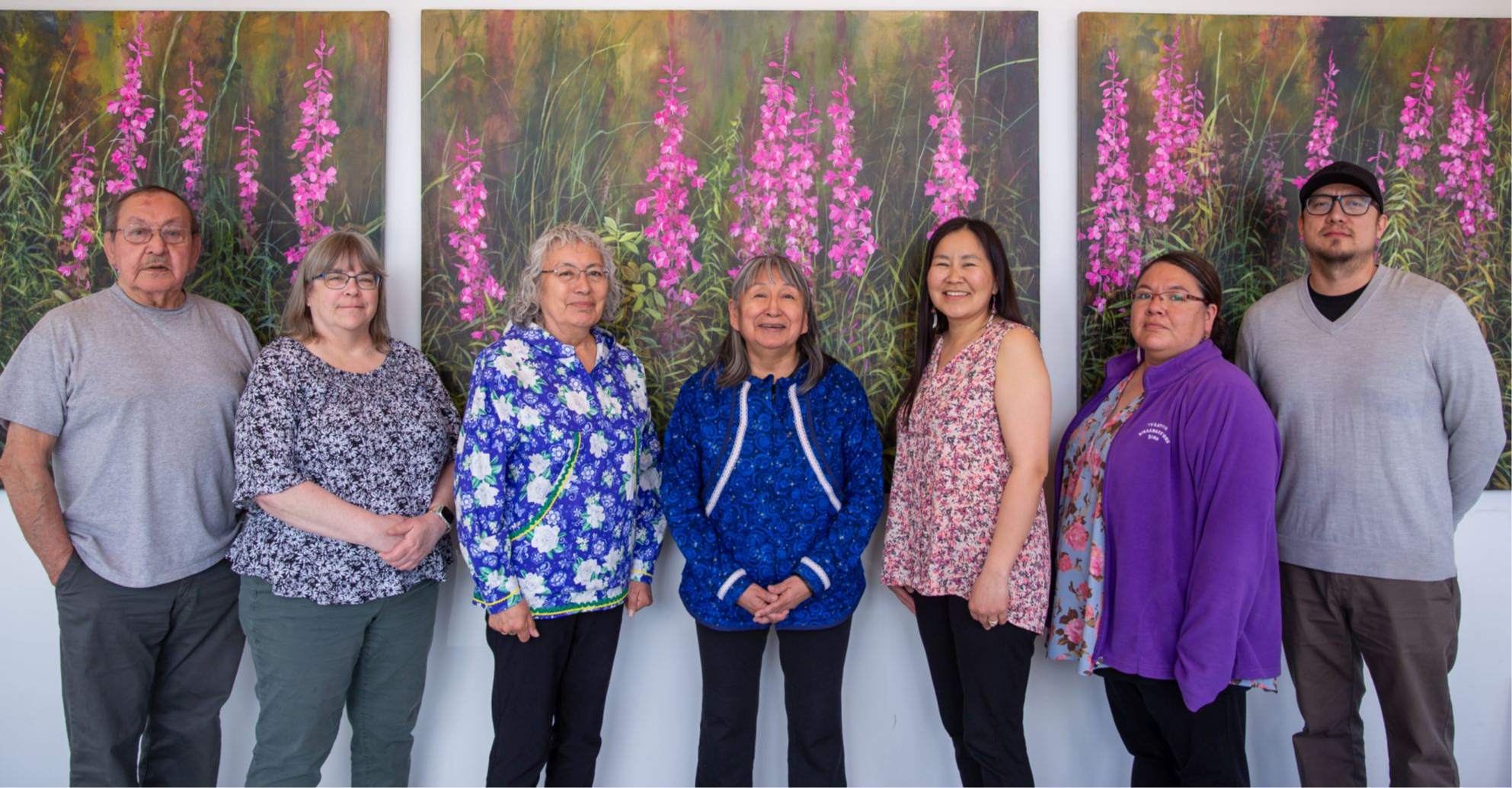 Seven YKSD board members posing in front of paintings of wildflowers.