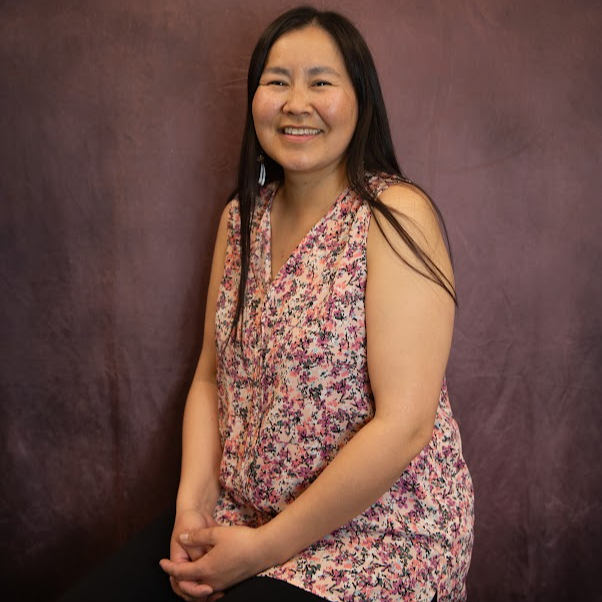 Woman in floral sweater poses against purple backdrop.