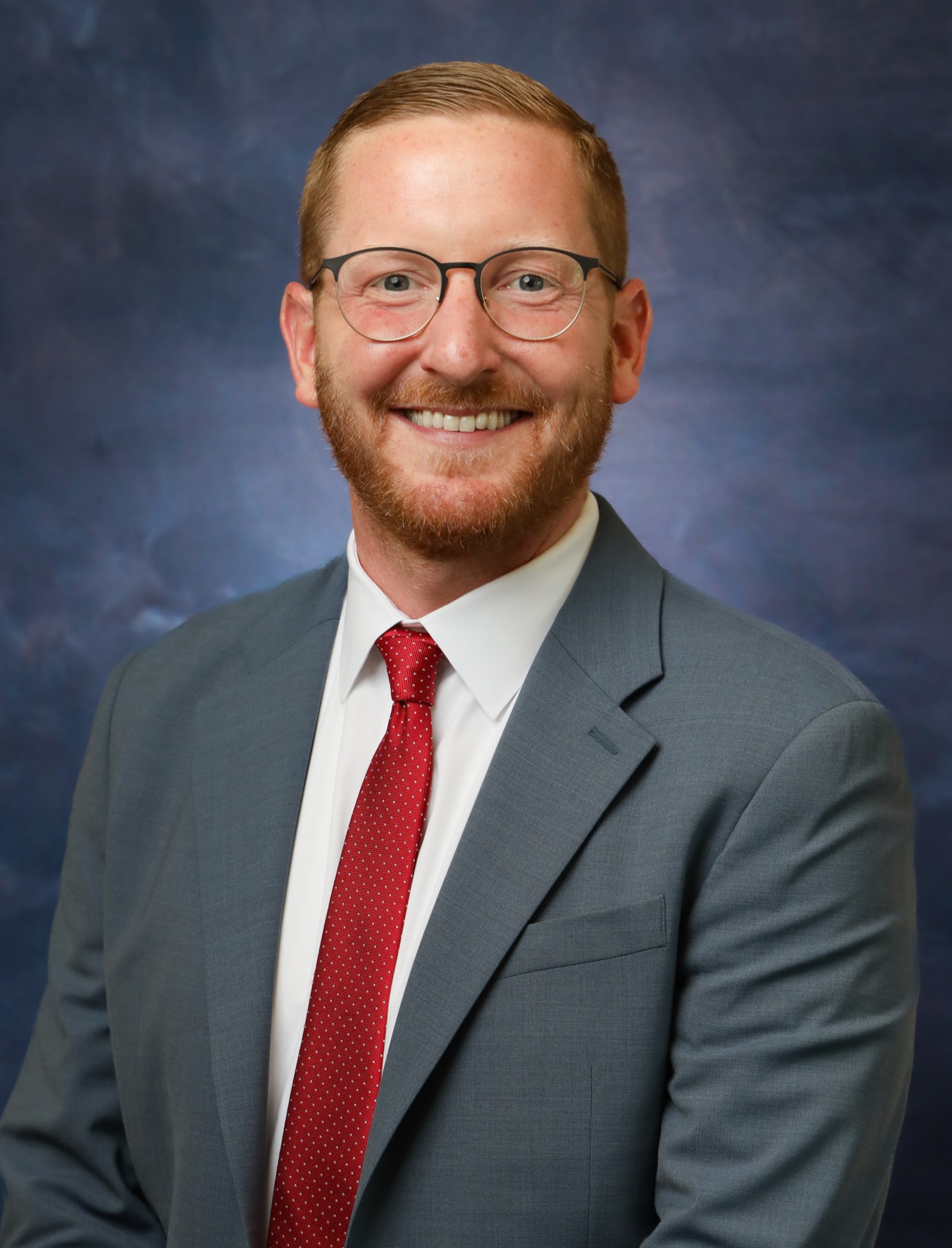 Man with glasses in a grey suit wearing a red tie. 