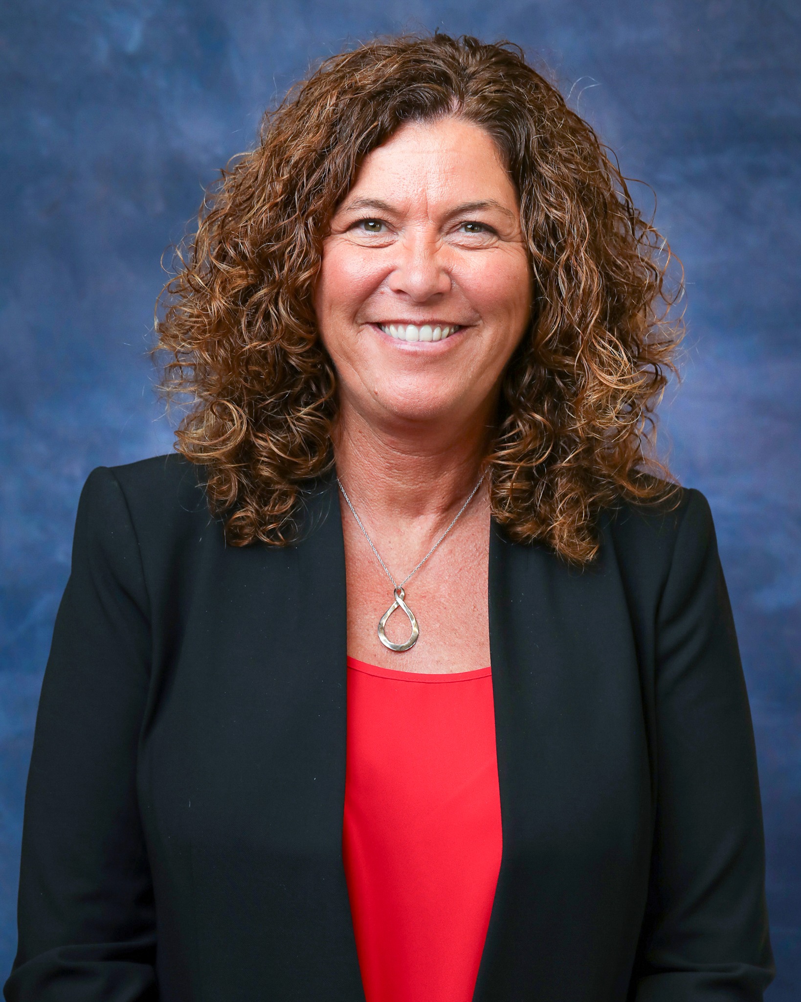 A woman with curly hair in a black blazer and a red shirt 