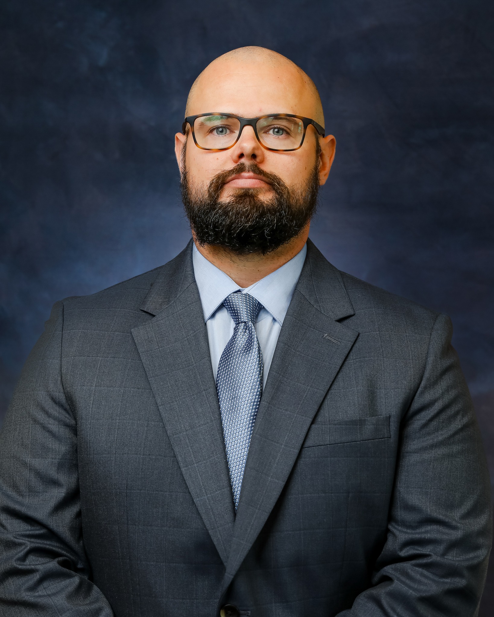 A bald man with thick frame glasses and a dark beard