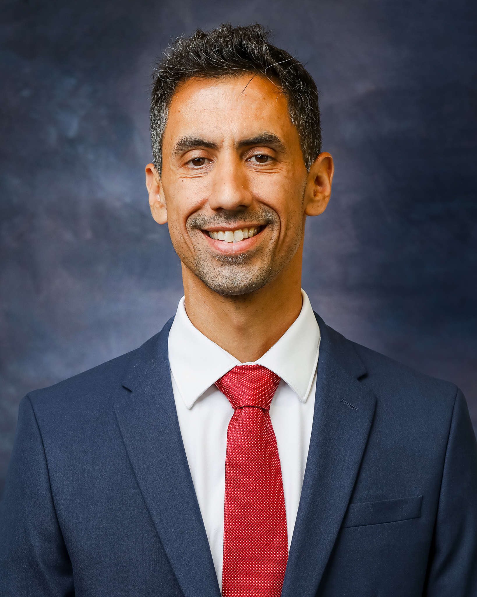 A tan man with a blazer and red tie. 