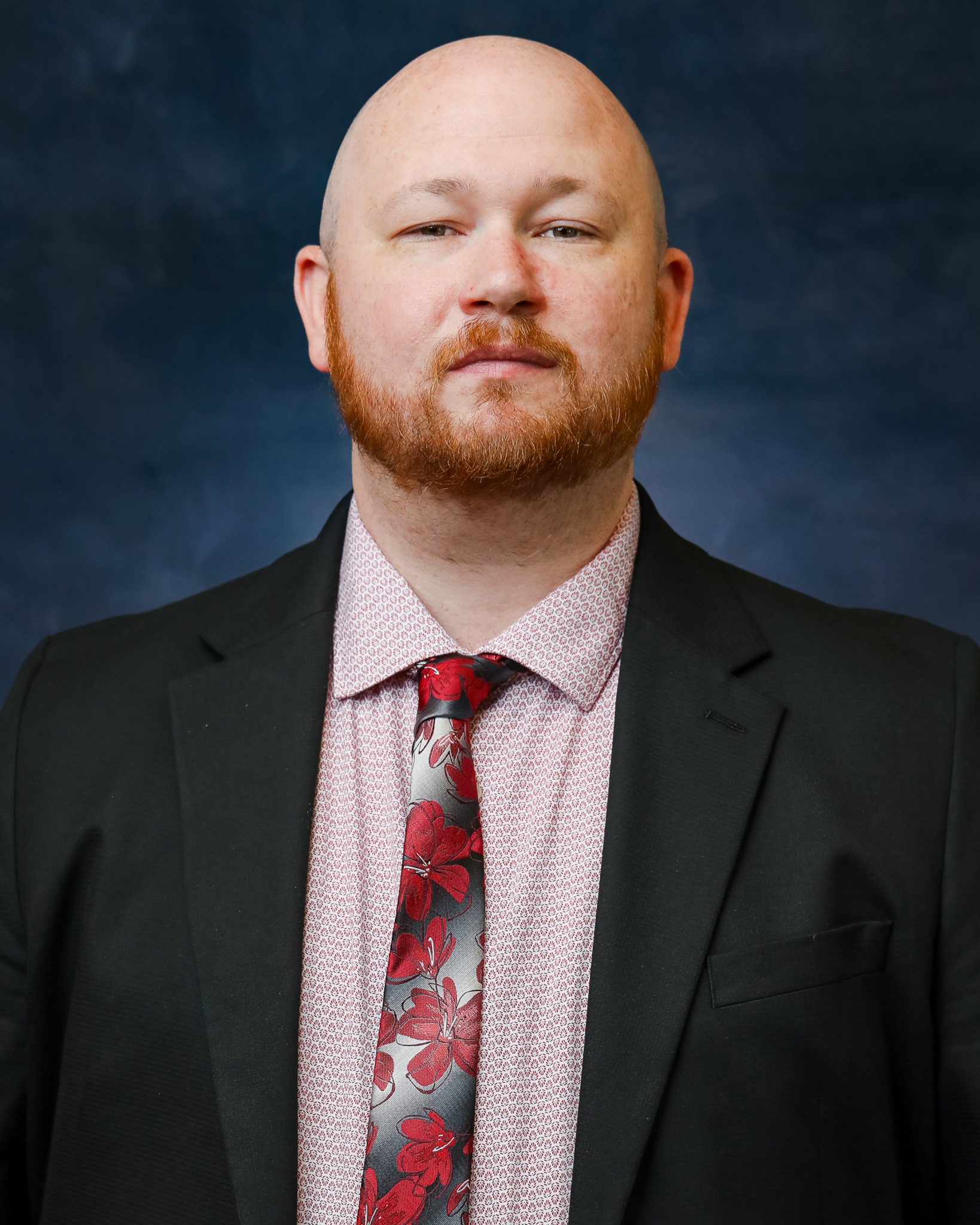 A bald man with a floral shirt and tie