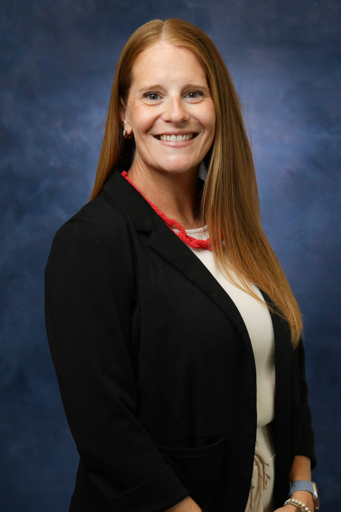 Woman with Red hair and a black blazer with a large orange necklace