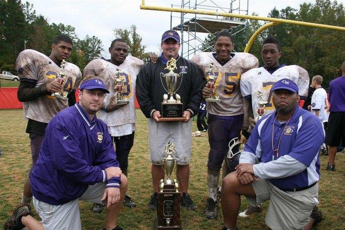 coach holding a trophy in the middle of his football players