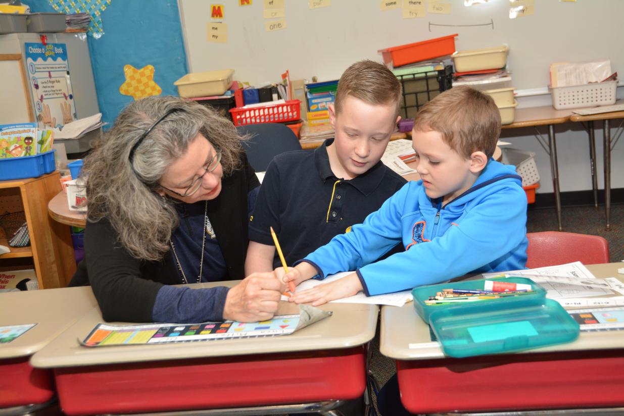 student working with a teacher that is kneeling near a desk