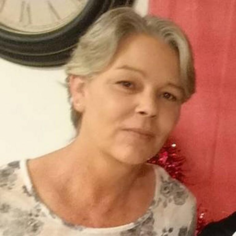 A woman with short gray hair wearing a floral top, standing indoors near a red wall and a clock.