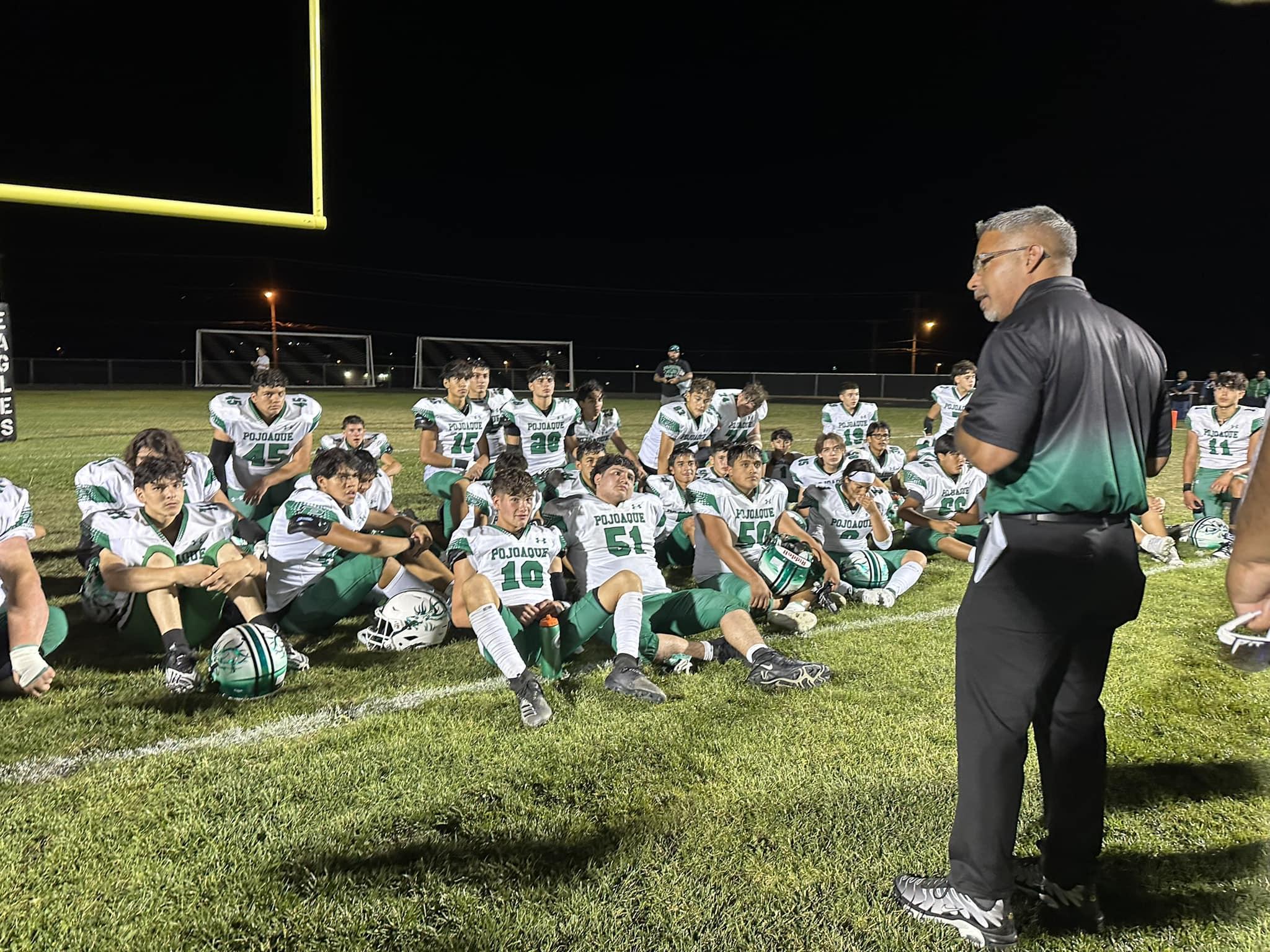A football coach giving instructions to a team of young players on a field at night.