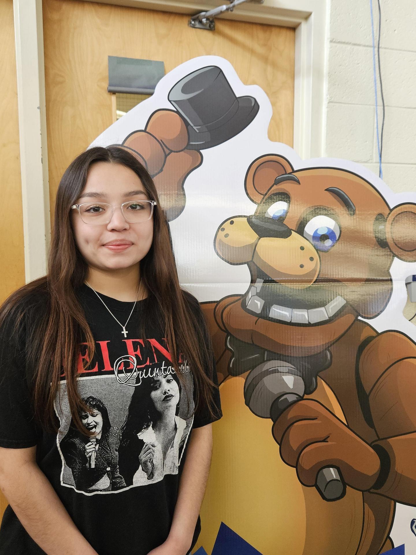 A girl with glasses and long hair stands next to a cartoon bear holding a hammer.