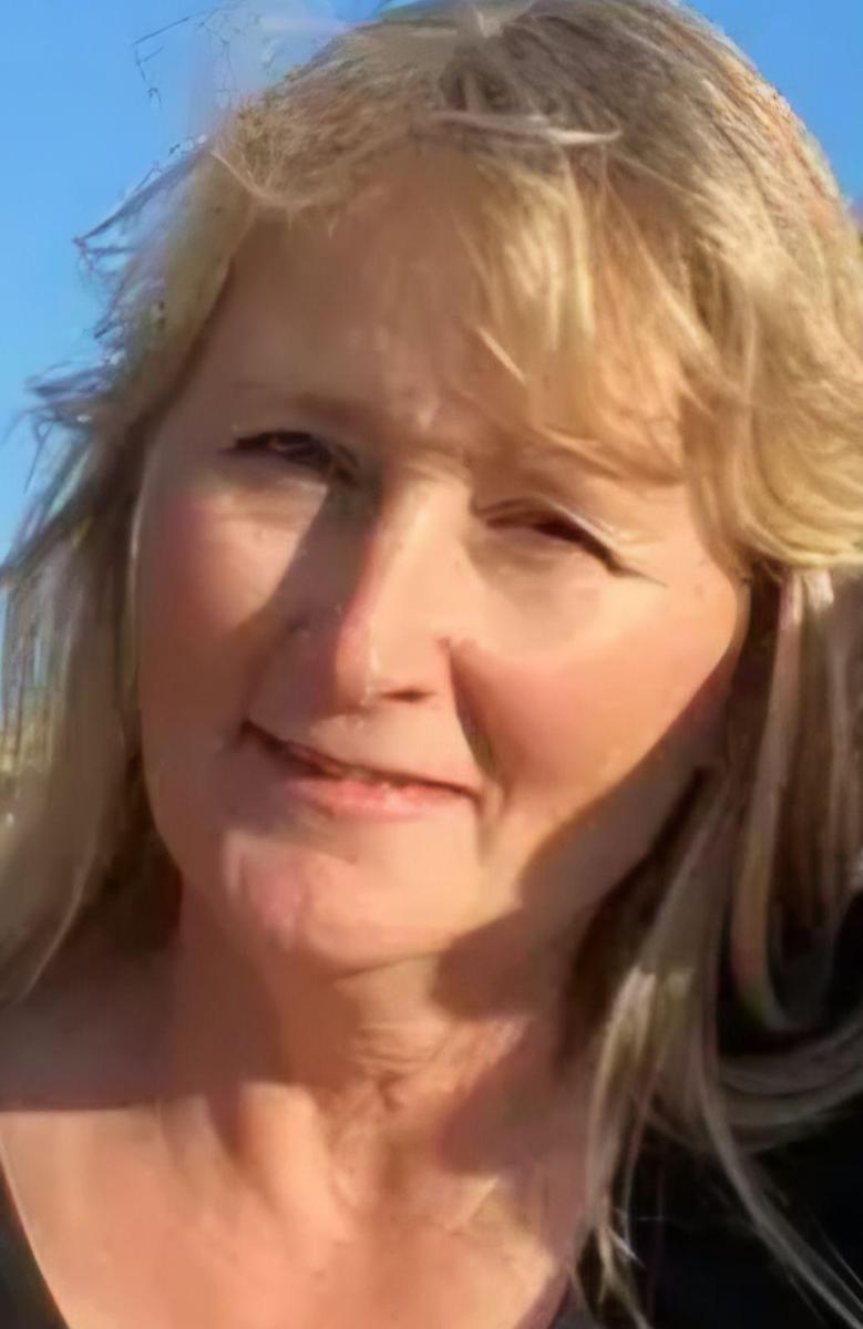 A woman with blonde hair and a slight smile, outdoors with a clear blue sky in the background.