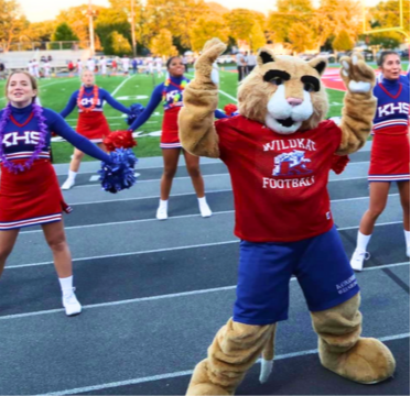 Cat mascot with cheerleaders on football field