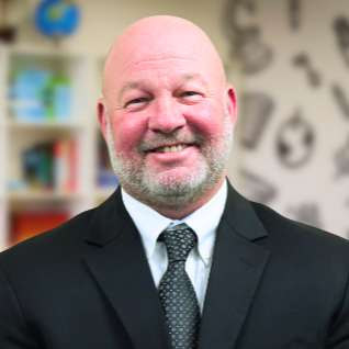 Adult male  principal smiling in suit and tie with classroom background