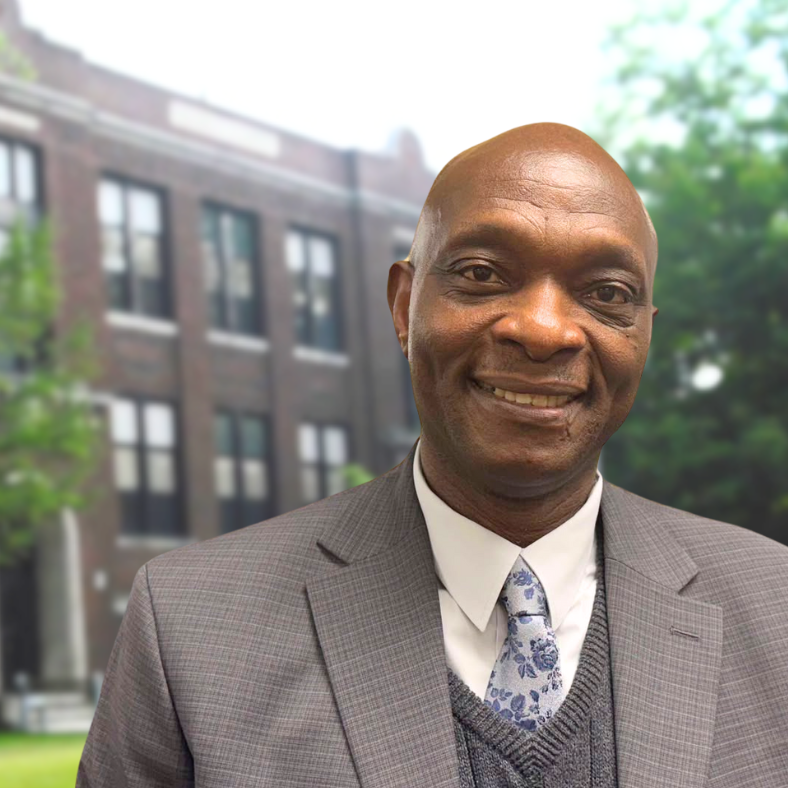 Man smiling and wearing suit and tie in front of school building
