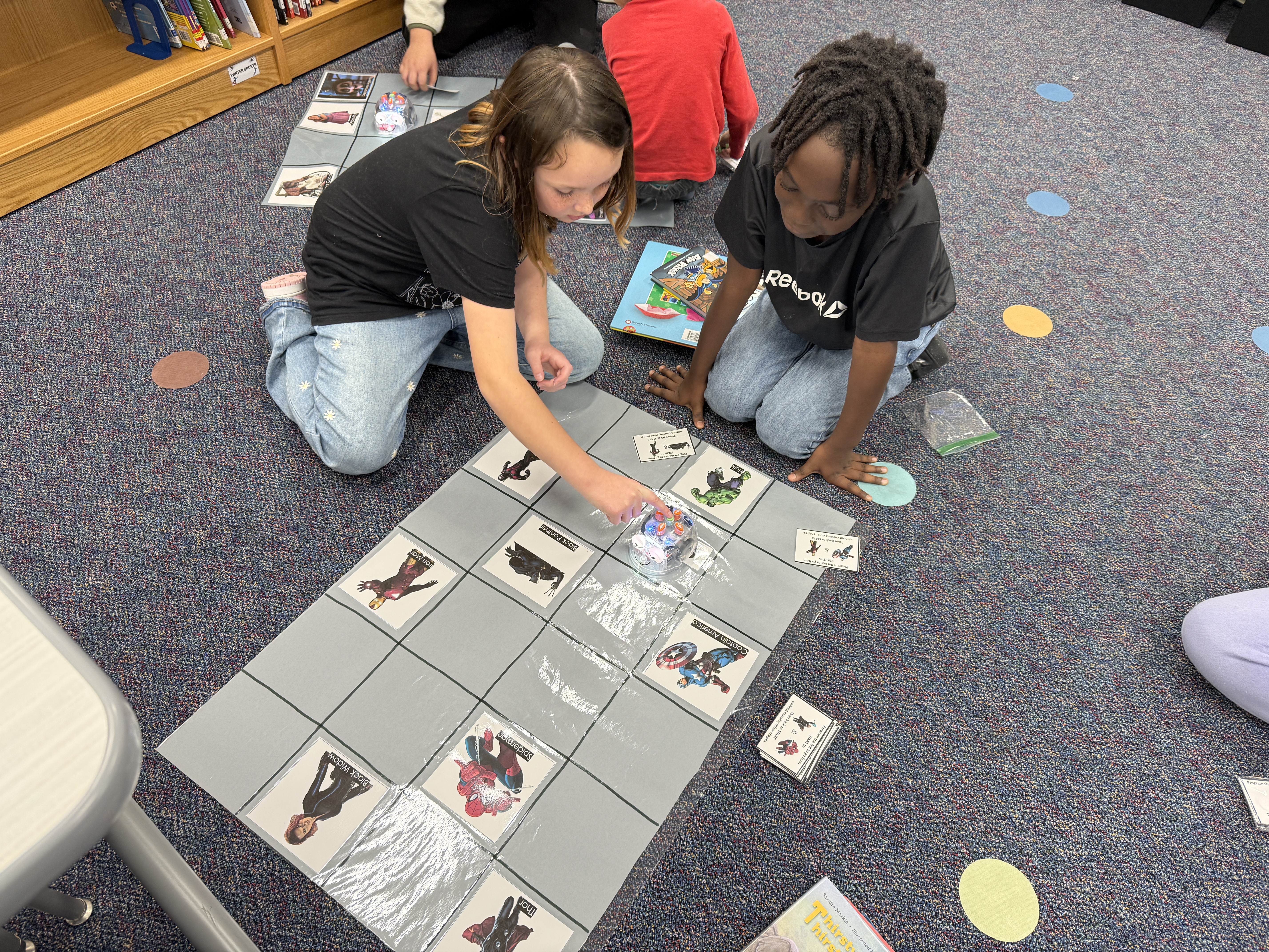 Two students working on coding using a grid mat and a Blue-Bot robot.