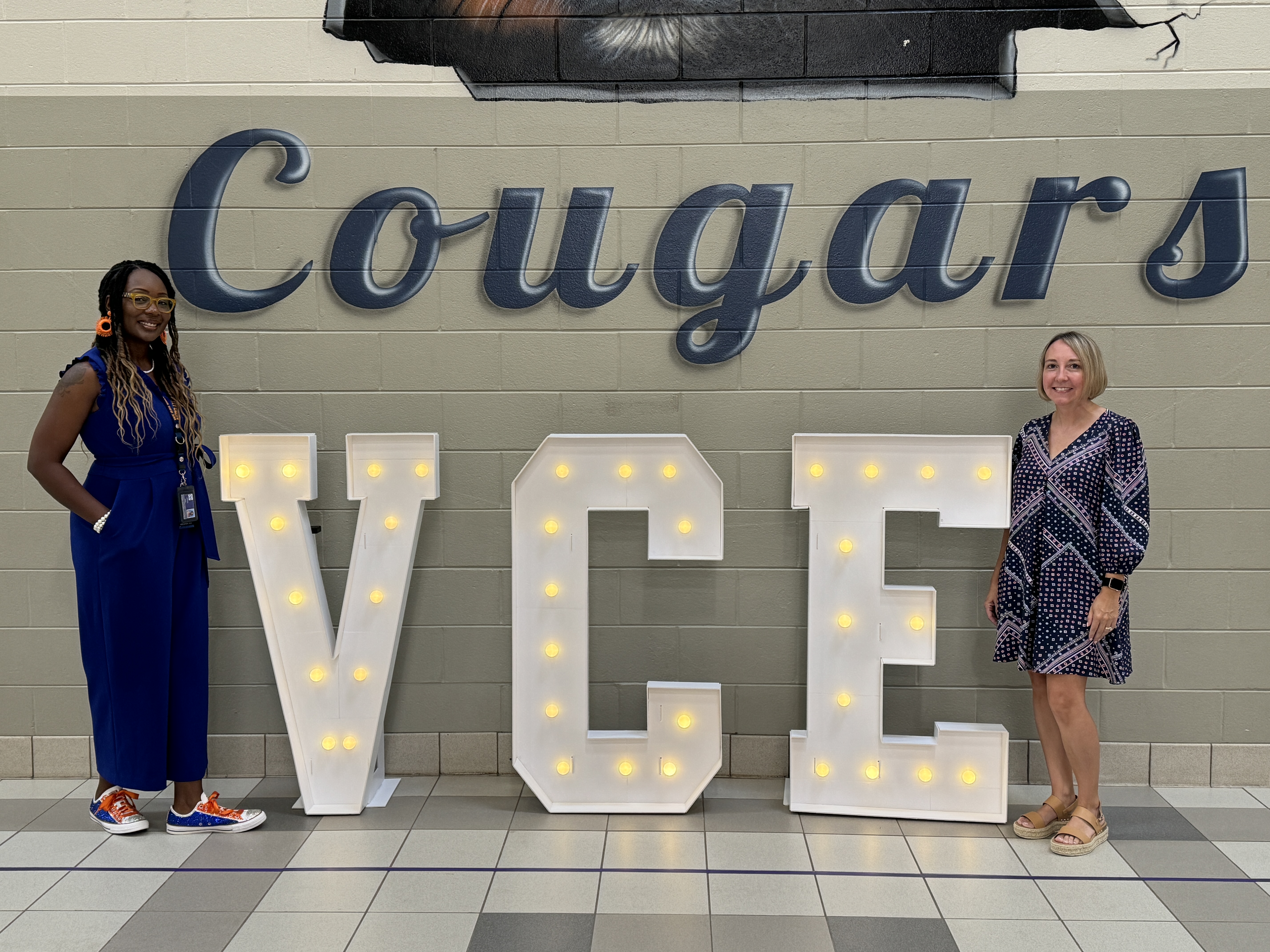 principal and assistant principal standing under cougar mural