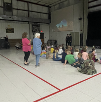 Group of kids gathered on gym floor, engaged in discussion.