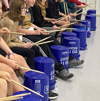 A diverse group of individuals sitting on the floor, engrossed in playing drums together.