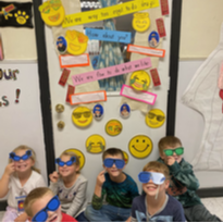 Children wearing sunglasses and holding up pictures, smiling and posing for a photo.