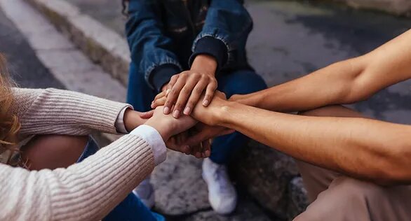 Three friends sitting on the ground, linking hands.