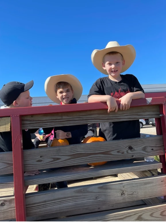 Three boys in cowboy hats sitting on a wooden bench outdoors.