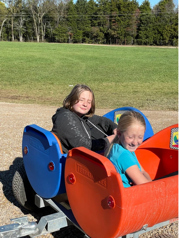 Two girls happily riding a small blue and orange train.