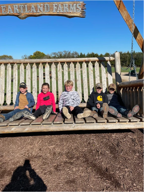 Five children happily swinging together at a playground.