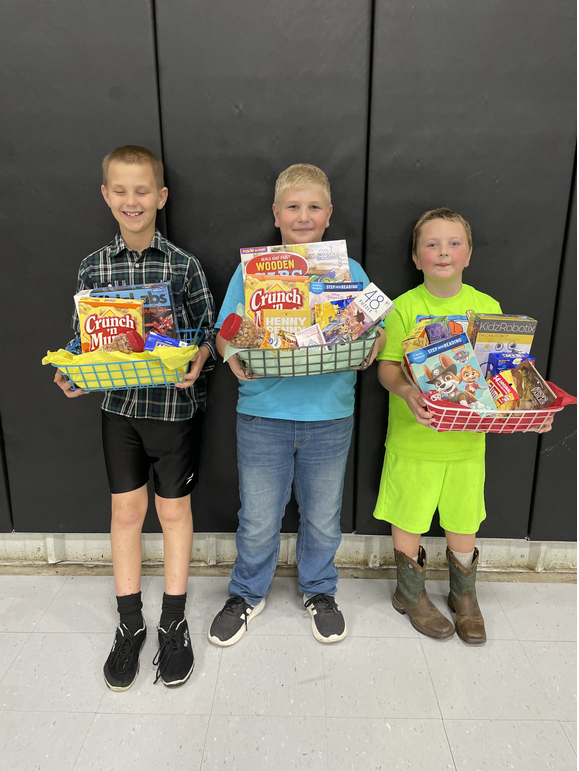 Three young boys holding baskets of food in front of a black wall