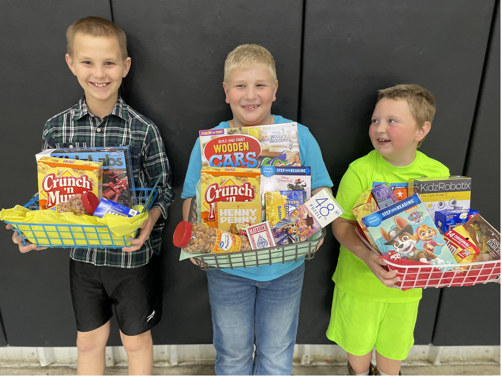 Three young boys holding baskets of food in front of a black wall