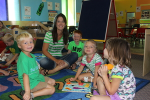 teacher sits on carpet with students