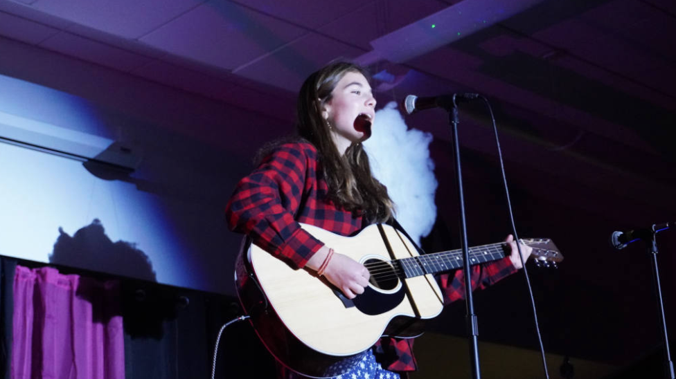 A talented girl singing into a microphone while strumming an acoustic guitar with passion and skill.