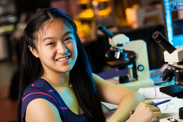 A young woman smiling at a desk with a microscope.