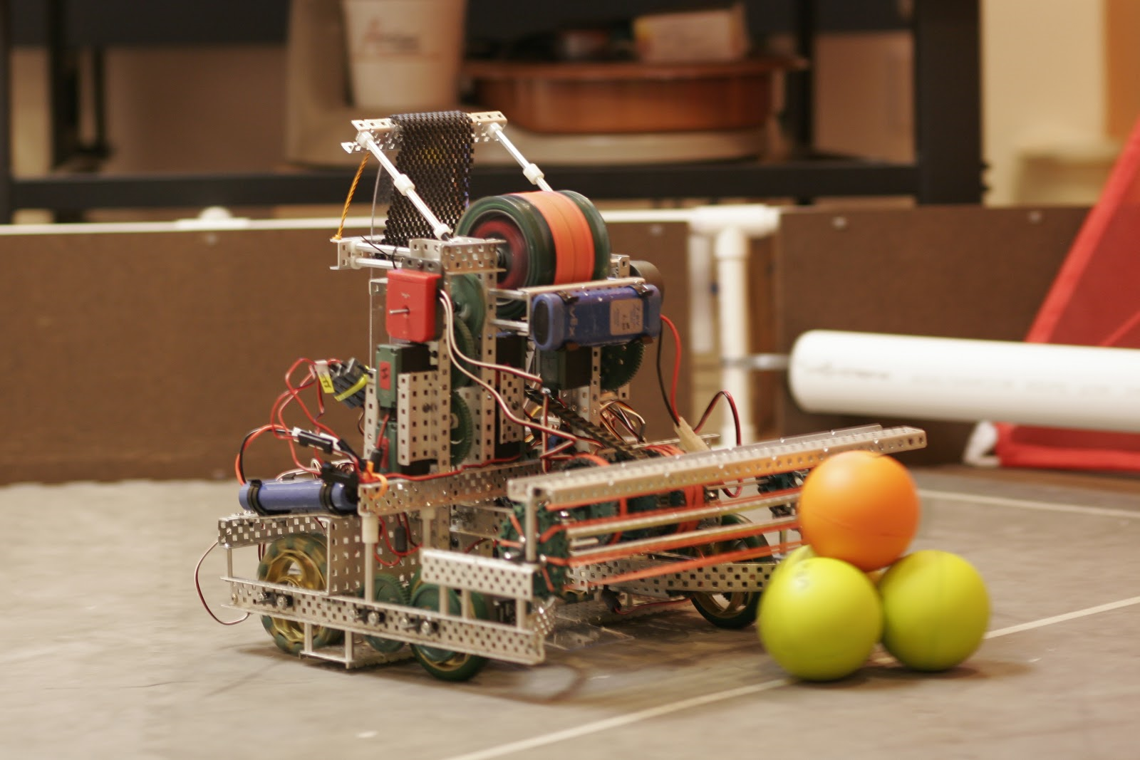 An image of a robot holding a ball with two balls on the ground.