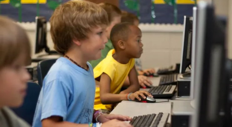 Children sitting at desks in a classroom, focused on computer screens.