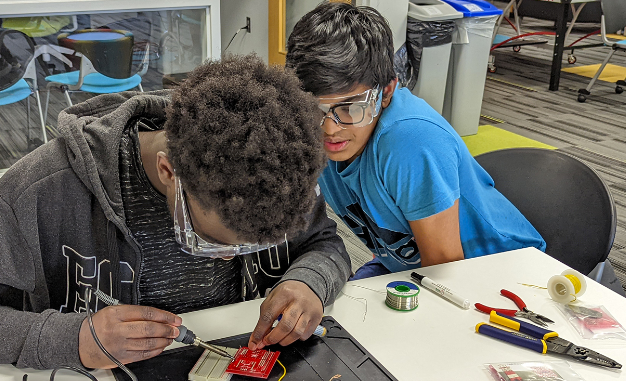 Two young men focused on electronics in a classroom, collaborating on a project together.