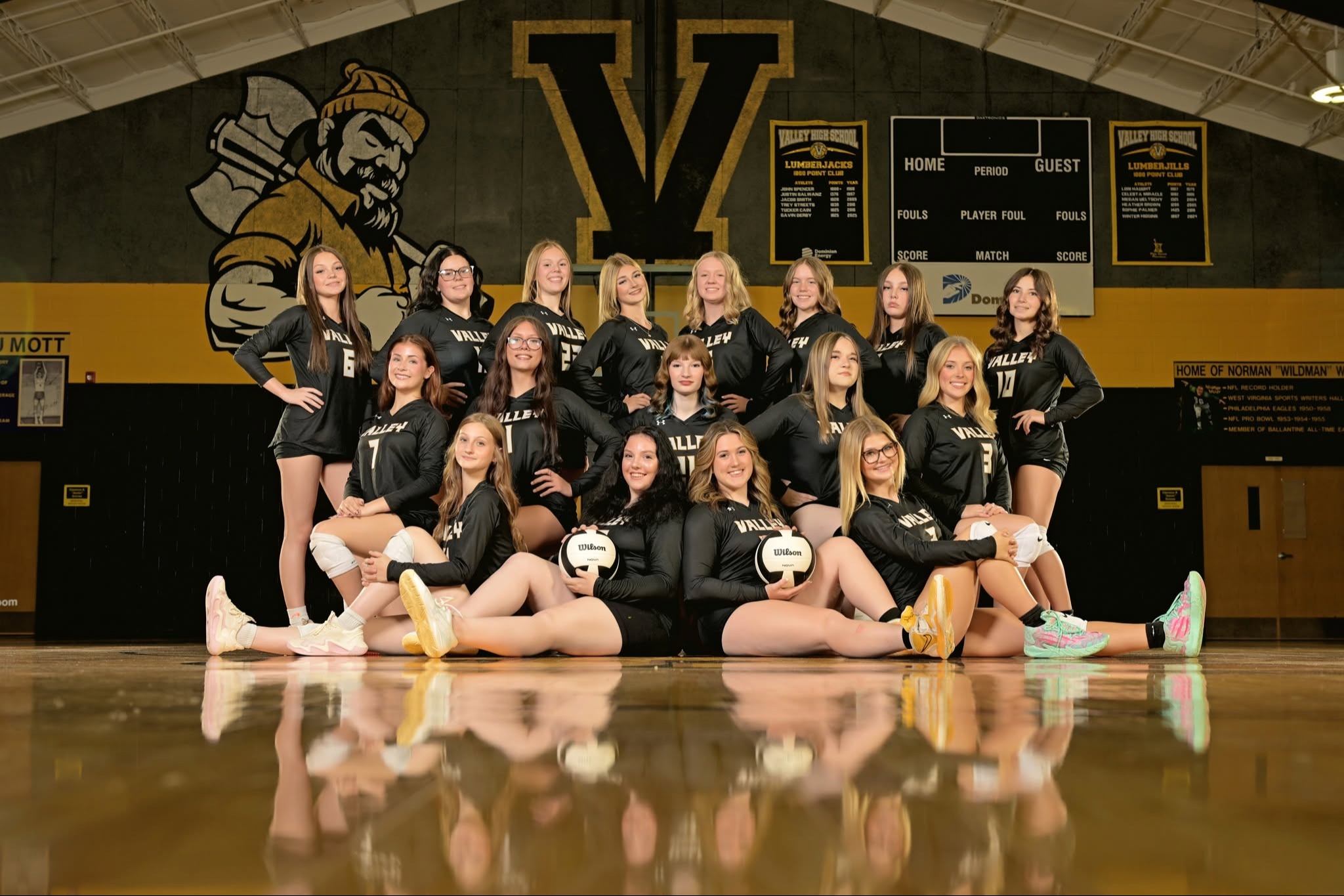 A group of women wearing black volleyball uniforms pose for a photo on a court.