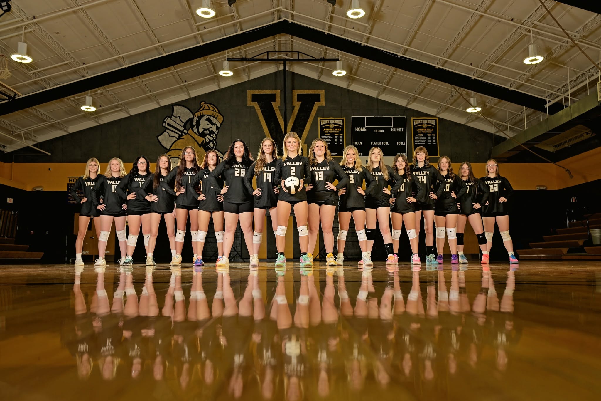 Volleyball team in matching uniforms, standing on a court with a reflection on the floor.
