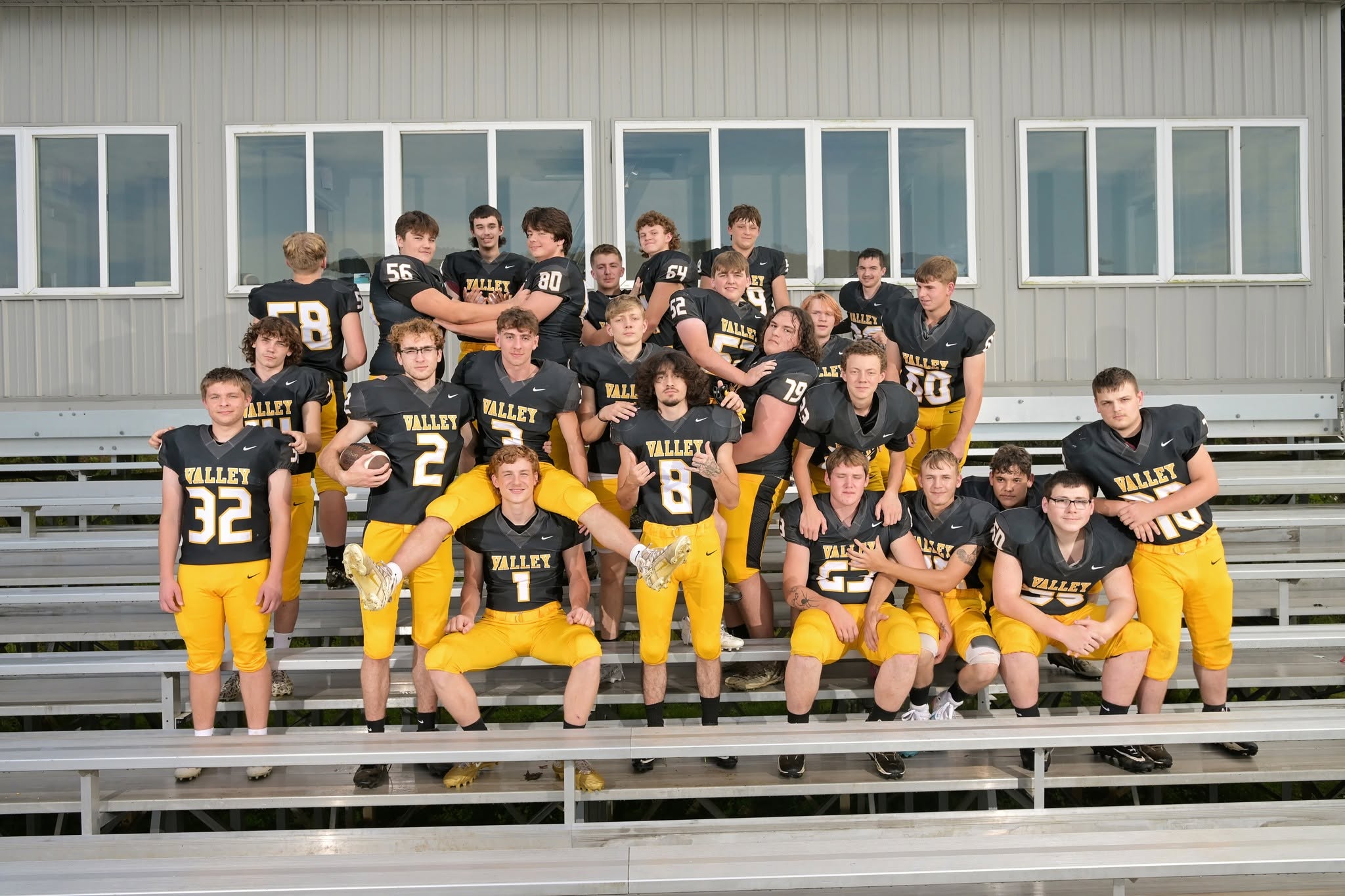 A group of young football players in black and yellow uniforms, sitting on bleachers.