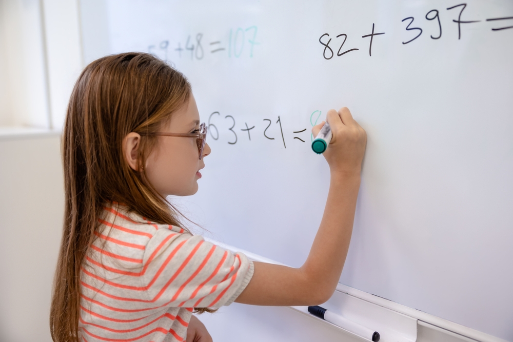 Girl standing at marker board doing a math problem