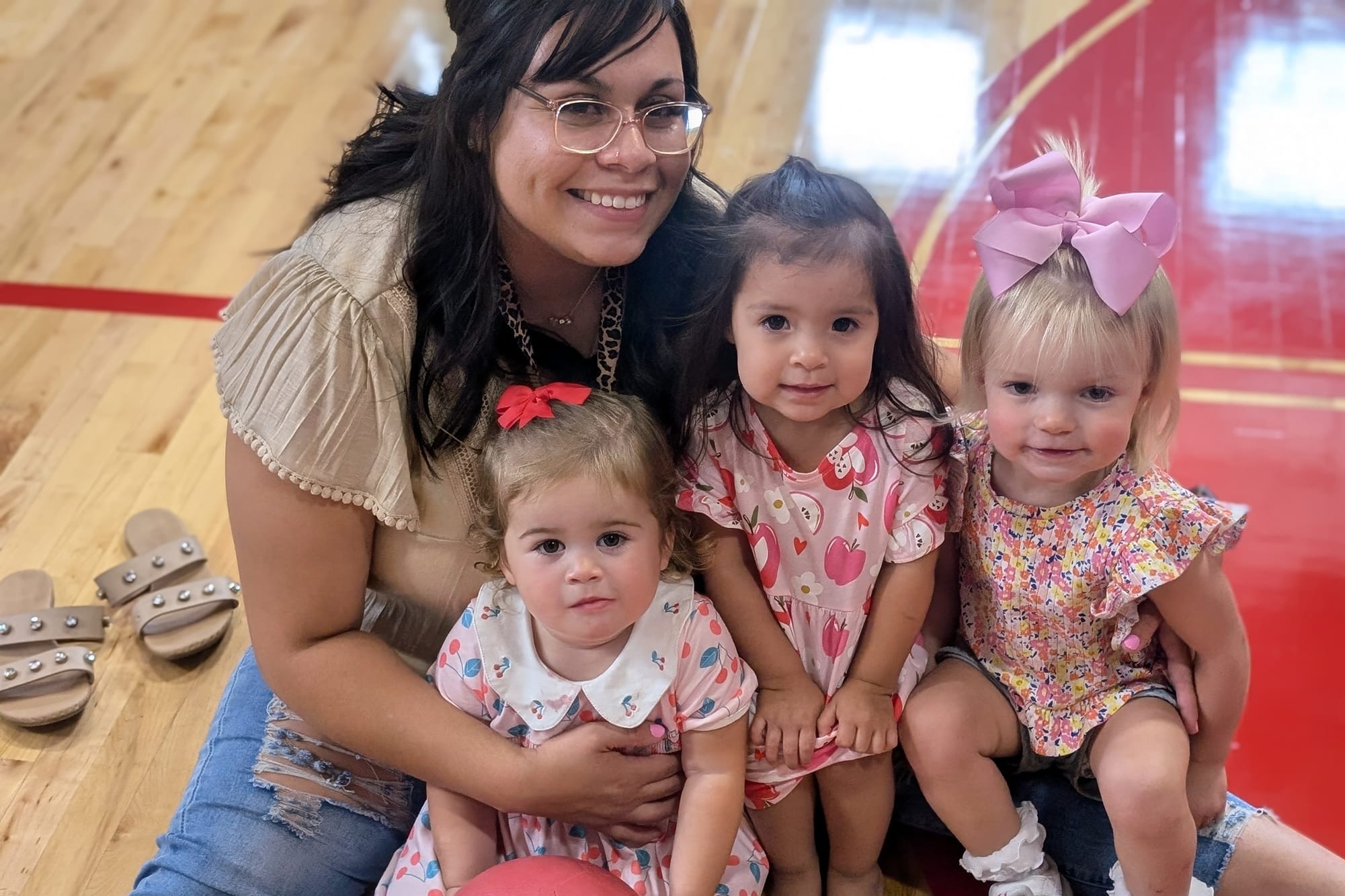 A teacher and her three smiling students sitting in the gym of  Bright Beginnings Daycare